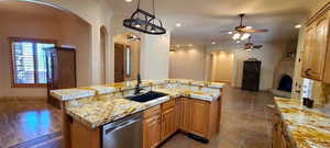 Kitchen featuring sink, stainless steel dishwasher, a kitchen island with sink, and light stone counters