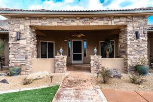 Property entrance featuring beautiful stonework, a tiled roof, and ceiling fan and planting beds.