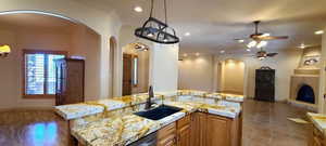 Kitchen with an island with sink, sink, light stone counters, and ceiling fan