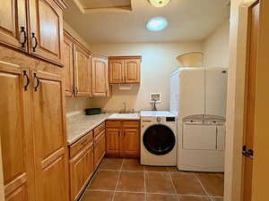 Washroom with washer and dryer, sink, a textured ceiling, cabinets, and dark tile patterned floors