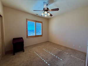 Empty room featuring a textured ceiling, carpet, and ceiling fan