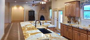 Kitchen with ceiling fan, sink, tasteful backsplash, and light stone countertops