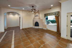 open concept family area with arched walkways, gas fireplace kiva, lighted ceiling fan, tile flooring, door to back patio and recessed lighting