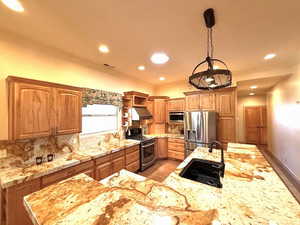 Kitchen with appliances with stainless steel finishes, hanging light fixtures, backsplash, sink, and a kitchen island with sink