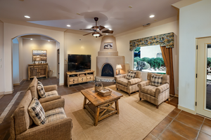 Virtually staged grand living area with arched walkways, gas fireplace kiva, lighted ceiling fan, tile flooring, door to back patio and recessed lighting
