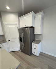 Kitchen with white cabinets, light wood-type flooring, stainless steel fridge, and tasteful backsplash