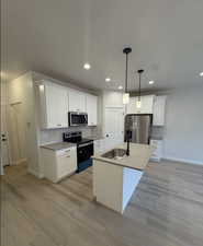 Kitchen with white cabinetry, a kitchen island with sink, hanging light fixtures, stainless steel appliances, and sink