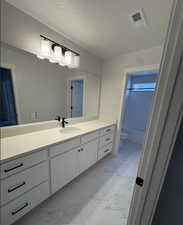 Bathroom with a textured ceiling, toilet, and vanity