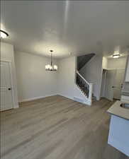 Unfurnished dining area with light hardwood / wood-style flooring, a chandelier, and a textured ceiling