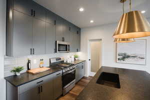 Kitchen with hanging light fixtures, sink, backsplash, wood-type flooring, and appliances with stainless steel finishes