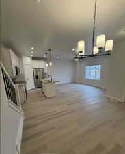 Kitchen with a center island with sink, sink, pendant lighting, stainless steel fridge with ice dispenser, and white cabinets