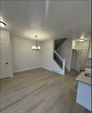 Unfurnished dining area featuring a textured ceiling, a notable chandelier, and light hardwood / wood-style flooring