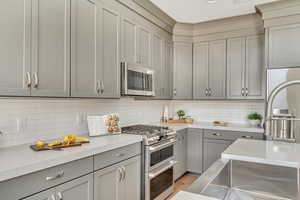 Kitchen with appliances with stainless steel finishes, light stone countertops, gray cabinetry, and decorative backsplash