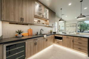 Kitchen featuring wine cooler, sink, backsplash, light brown cabinetry, and pendant lighting