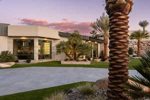 Back house at dusk featuring a patio area and a lawn