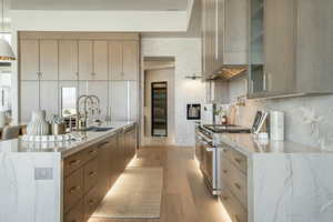 Kitchen with light hardwood / wood-style flooring, high end stainless steel range oven, wall chimney exhaust hood, decorative backsplash, and sink