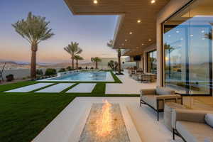 Pool at dusk featuring a yard, a mountain view, a patio area, and an outdoor living space with a fire pit