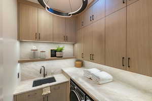 Kitchen with decorative backsplash, sink, light brown cabinetry, and washer / dryer