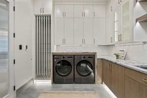 Laundry area with light tile patterned flooring, cabinets, and washing machine and clothes dryer