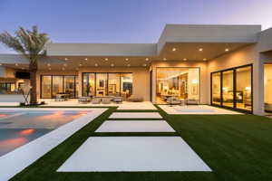 Back house at dusk featuring outdoor lounge area, a lawn, and a patio area