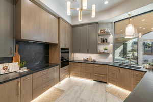 Kitchen with hanging light fixtures, sink, backsplash, black electric cooktop, and light brown cabinetry