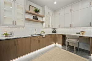 Kitchen featuring light stone counters, decorative backsplash, light tile patterned floors, sink, and white cabinetry