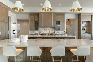 Kitchen with backsplash, a large island, a kitchen bar, and light stone countertops