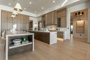 Kitchen featuring light hardwood / wood-style floors, hanging light fixtures, a large island with sink, and backsplash