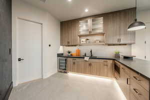 Kitchen with hanging light fixtures, light brown cabinets, backsplash, beverage cooler, and sink