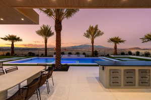 Pool at dusk featuring a patio area, exterior bar, a mountain view, and a hot tub