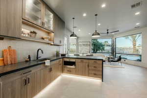 Kitchen with light brown cabinetry, decorative light fixtures, decorative backsplash, sink, and kitchen peninsula