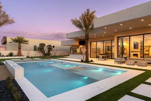 Pool at dusk featuring a patio and an outdoor living space with a fireplace