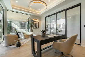 Office area with a tray ceiling, french doors, and light wood-type flooring