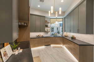 Kitchen featuring light brown cabinetry, pendant lighting, gray cabinetry, and decorative backsplash