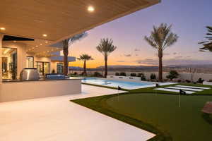 Pool at dusk with an in ground hot tub, a patio, an outdoor kitchen, and grilling area