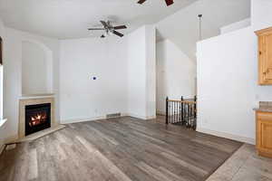 Unfurnished living room with a fireplace, a towering ceiling, ceiling fan, and light hardwood / wood-style flooring