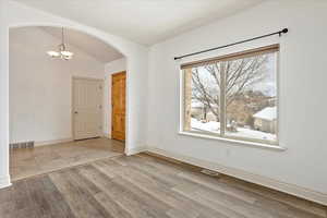 Unfurnished room featuring light hardwood / wood-style floors, vaulted ceiling, and a notable chandelier