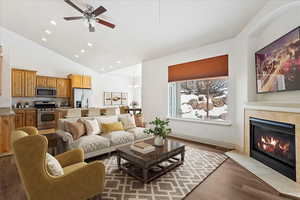 Living room with baseboards, a tiled fireplace, light wood-style flooring, ceiling fan with notable chandelier, and recessed lighting