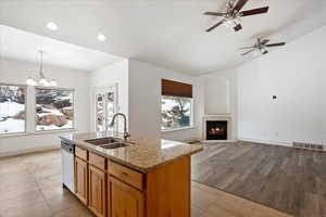 Kitchen featuring hanging light fixtures, an island with sink, light stone counters, stainless steel dishwasher, and sink