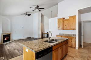 Kitchen featuring sink, dishwasher, high vaulted ceiling, light stone countertops, and a kitchen island with sink