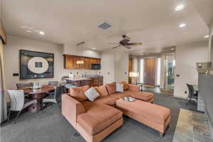 Living room with ceiling fan, dark colored carpet, and sink