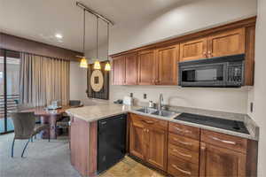 Kitchen with hanging light fixtures, black appliances, kitchen peninsula, sink, and light colored carpet