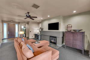 Living room with ceiling fan, a tile fireplace, and dark colored carpet