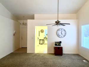 Empty room featuring light carpet, baseboards, visible vents, and ceiling fan with notable chandelier