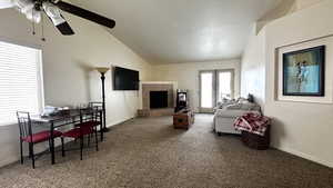 Living room with lofted ceiling, ceiling fan, a tile fireplace, carpet flooring, and baseboards