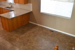 Kitchen with kitchen peninsula, sink, stainless steel dishwasher, light stone counters, and decorative backsplash