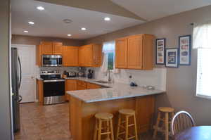 Kitchen featuring a kitchen bar, sink, stainless steel appliances, kitchen peninsula, and light stone countertops