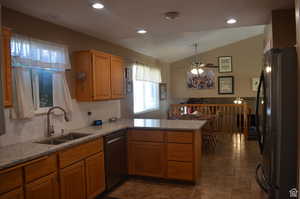 Kitchen featuring vaulted ceiling, sink, dishwasher, black fridge, and kitchen peninsula