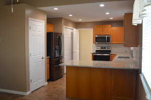 Kitchen featuring kitchen peninsula, stainless steel appliances, sink, light stone counters, and decorative backsplash