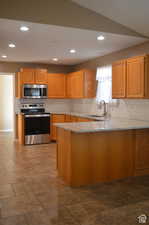 Kitchen featuring appliances with stainless steel finishes, sink, light stone countertops, and kitchen peninsula